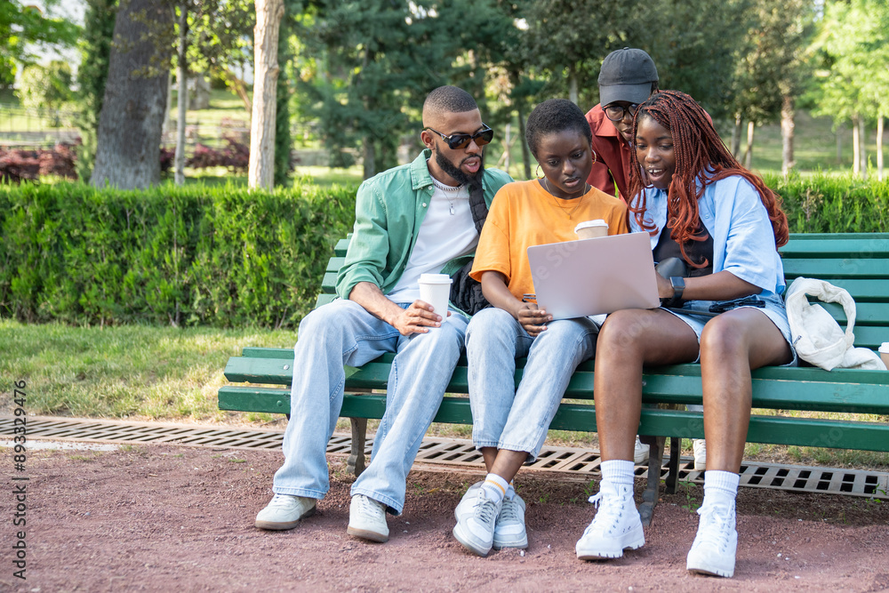 Group of happy African friends sit on park bench with laptop, discussing, sharing opinions discussing exam results. Black students relaxing in nature, spending time together. Students life concept Group of happy African friends sit on park bench with laptop, discussing, sharing opinions discussing exam results. Black students relaxing in nature, spending time together. Students life concept