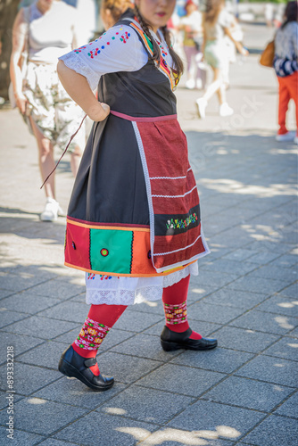 Woman in traditional Bulgarian folk costume tying an apron, city street