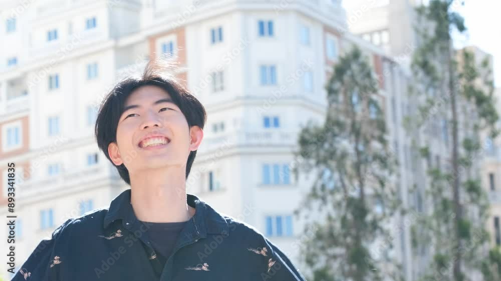 Asian young man is smiling and dancing in a city street. Scene is happy and carefree Asian young man is smiling and dancing in a city street. Scene is happy and carefree