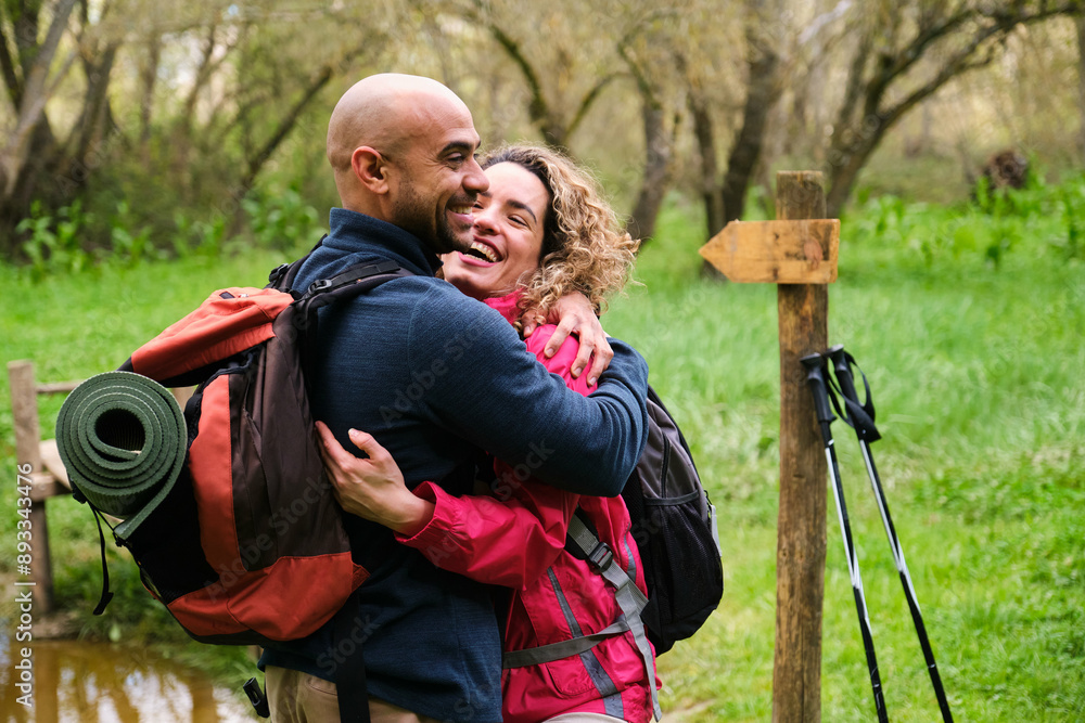 A man and woman hugging in a forest after trekking. The man is wearing a backpack they are laughing. A man and woman hugging in a forest after trekking. The man is wearing a backpack they are laughing.