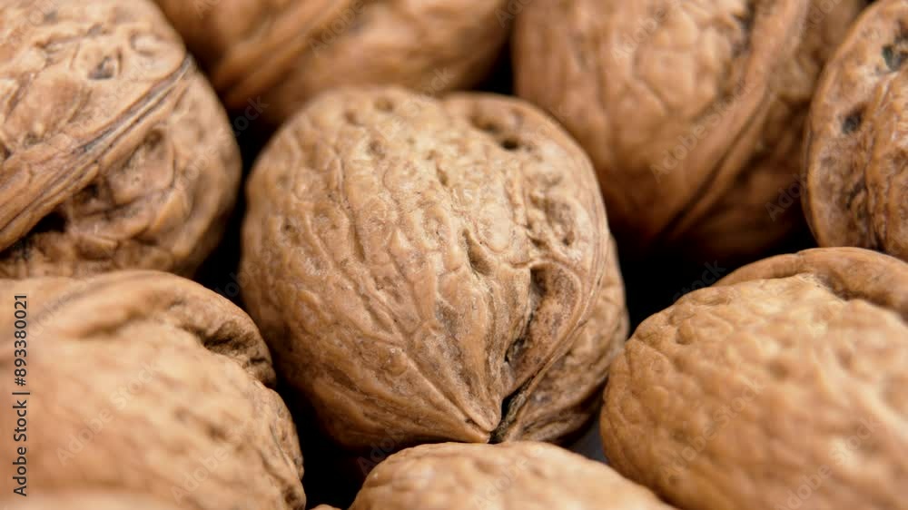 A walnut falls into a pile of whole unshelled nuts, their brown shell and textured surface highlighted closeup. Macro A walnut falls into a pile of whole unshelled nuts, their brown shell and textured surface highlighted closeup. Macro