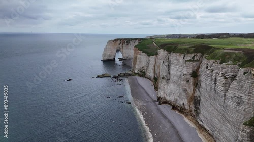 Landscape drone video of tall, steep limestone cliffs by the ocean with one with a hole in it creating an arch