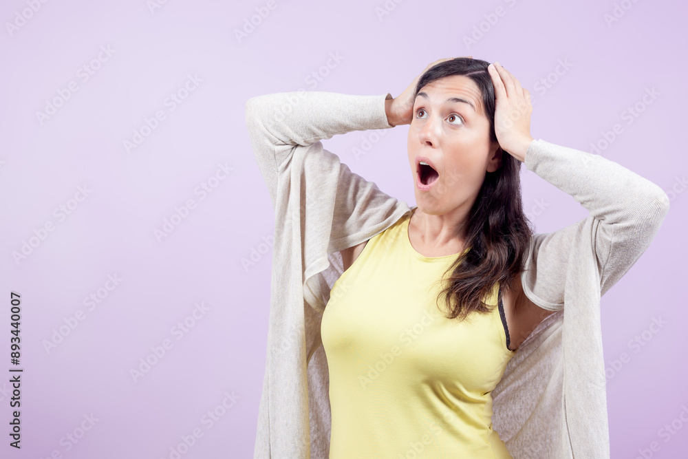 Naklejka premium Woman looks surprised to the side with hands on head isolated on lilac background. Concept of surprise and disbelief.