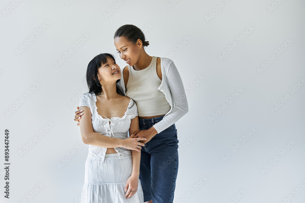 An interracial lesbian couple gazes lovingly at each other against a simple white background. An interracial lesbian couple gazes lovingly at each other against a simple white background.