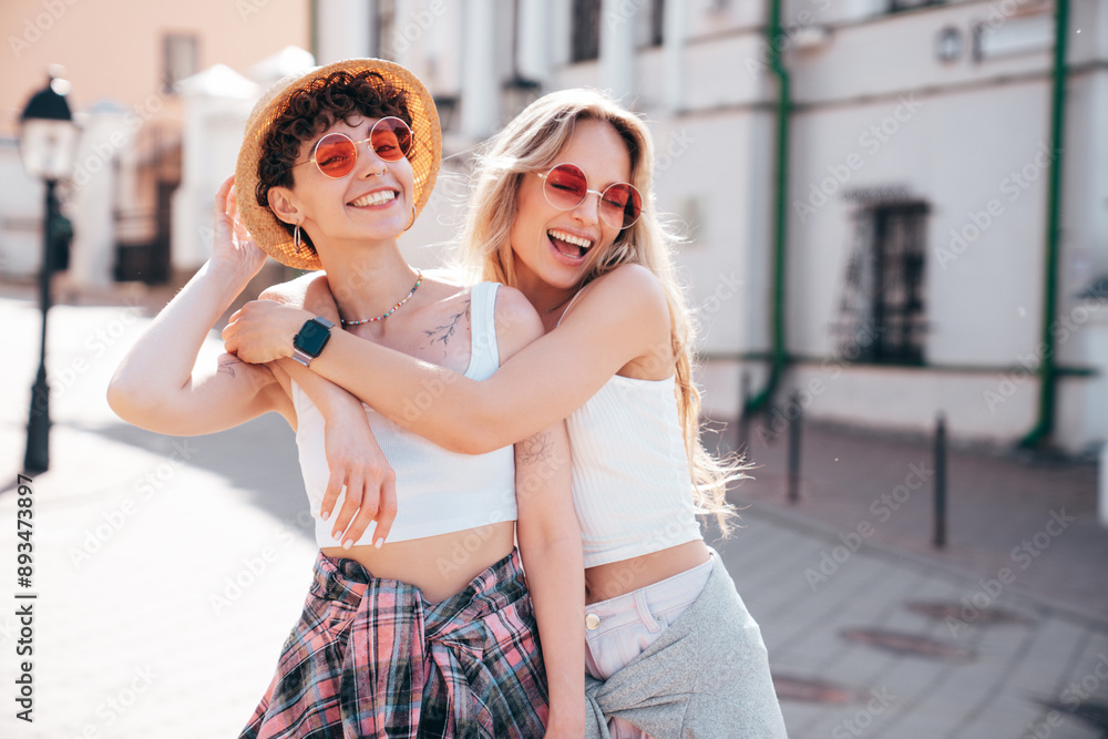 Naklejka premium Two young beautiful smiling hipster female in trendy summer white t-shirt and shorts clothes. Sexy carefree women posing in the street. Positive models having fun, hugging and going crazy