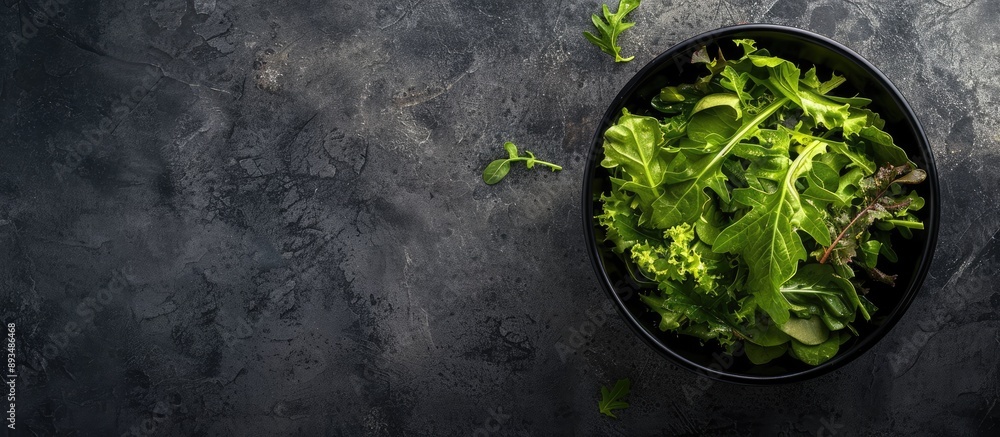 Top view of salad leaves mixed in a black bowl set against a backdrop of dark slate stone or concrete with an empty space for additional content in the image Top view of salad leaves mixed in a black bowl set against a backdrop of dark slate stone or concrete with an empty space for additional content in the image