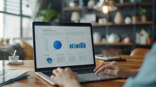 Person Reviewing Brochure Mockup on Laptop with Blurred Office Documents and Stationery in Background