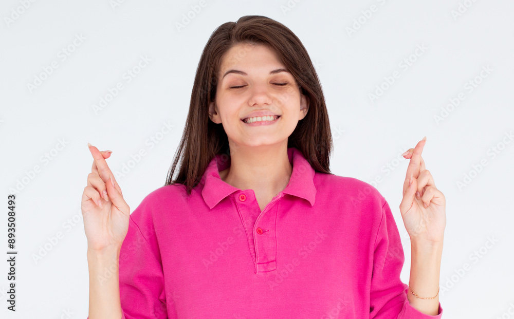 Intrigued woman in pink long sleeve praying with crossed fingers and closed eyes over white background Intrigued woman in pink long sleeve praying with crossed fingers and closed eyes over white background