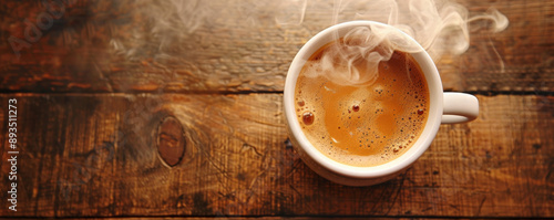 Top view of a steaming hot coffee cup placed on a rustic wooden table, with a beautiful crema swirling on top. The natural light highlights the rich brown hues of the coffee. photo