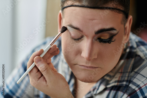 A queer person applies eyeshadow with a makeup brush.