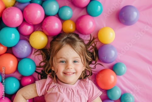 Cute Girl in a Pool of Colorful Balls, Laughing at Camera, Plain Pink Background