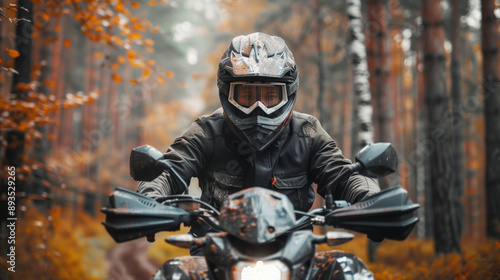 Motorcyclist in helmet and goggles riding on forest roads in autumn landscape on his quad bike.