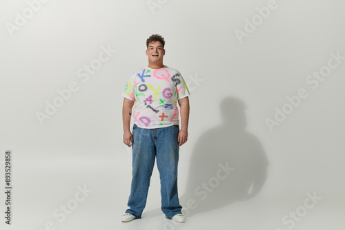 A queer person smiles brightly in a white shirt with colorful letters.