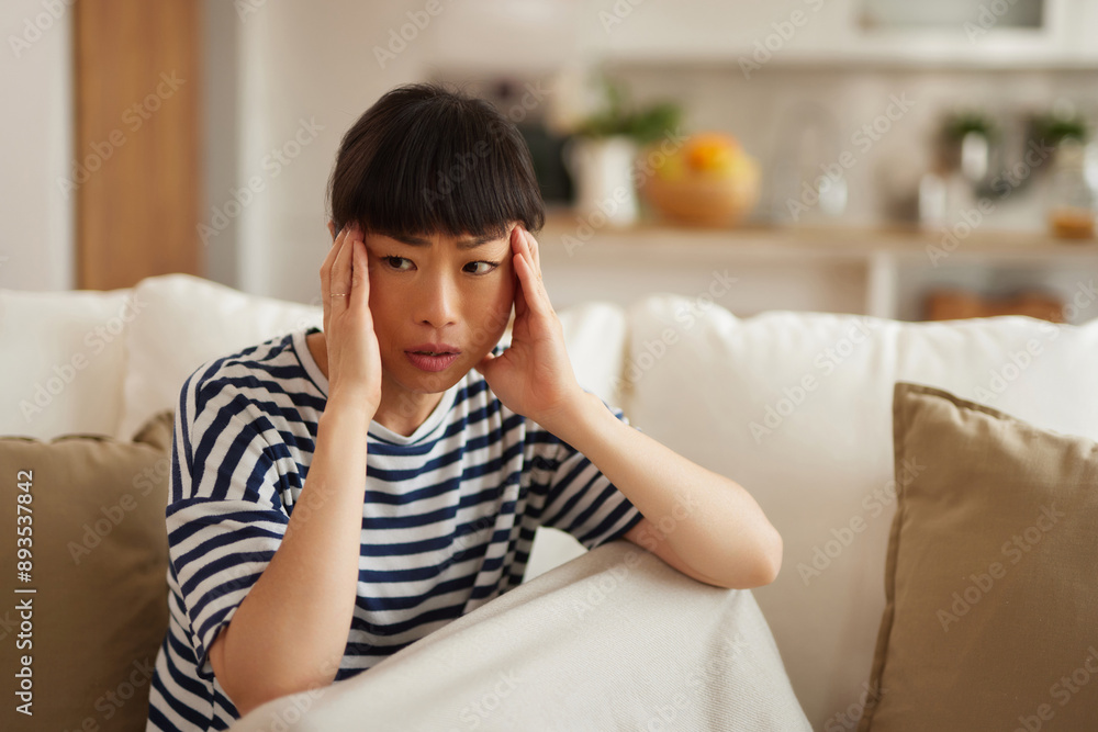 Woman holding head in hands while sitting on couch Woman holding head in hands while sitting on couch