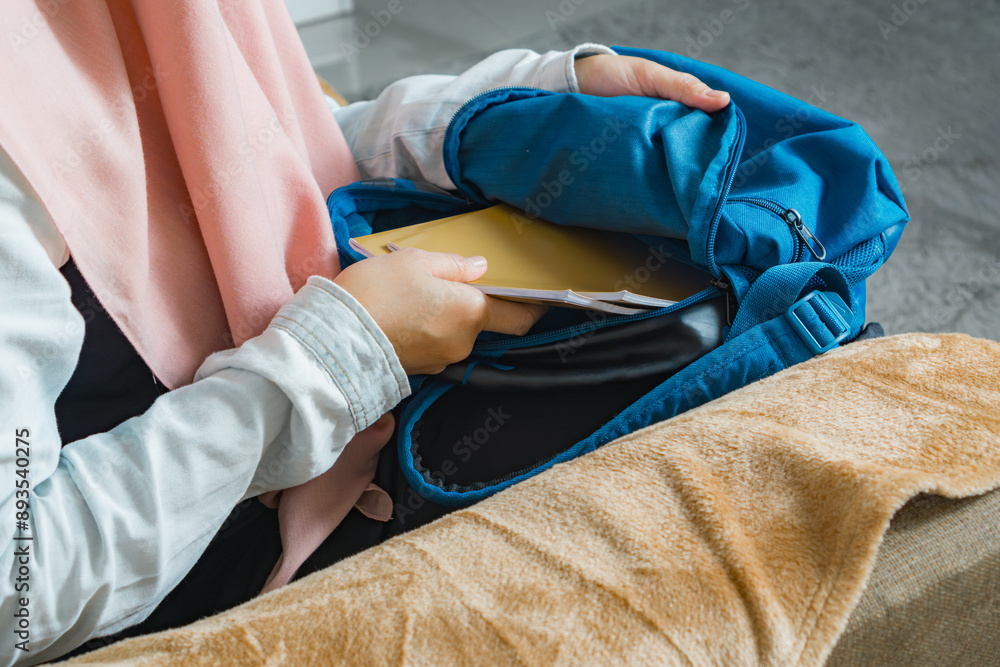 A mother prepares and packs her child's school supplies into their school bag A mother prepares and packs her child's school supplies into their school bag