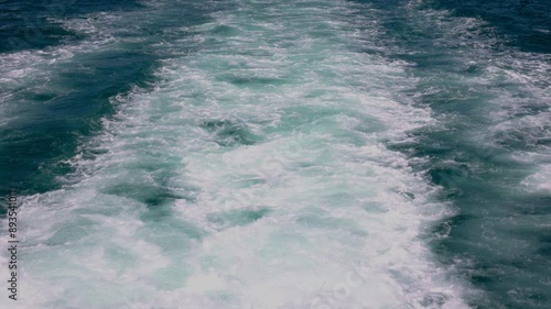 White foamy wake trails behind a boat in clear blue ocean water.