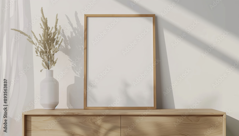 A blank wooden picture frame sits on a wooden cabinet beside a minimalist vase with green branches, bathed in natural sunlight. Perfect for showcasing simplicity and elegance. A blank wooden picture frame sits on a wooden cabinet beside a minimalist vase with green branches, bathed in natural sunlight. Perfect for showcasing simplicity and elegance.
