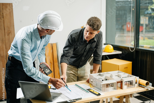 Professional collaboration in architecture. Two engineers work on construction plans, using tools like laptops, tablets, and scale models. photo