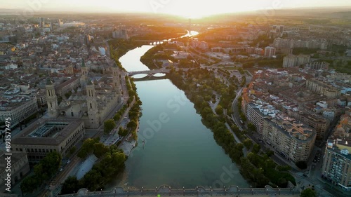 ZARAGOZA - Spain. Spectacular aerial view of historic and medieval city center of Zaragoza. Drone backwards above Ebro River. Spectacular orange sunset reflecting on buildings and landscape. Travel 