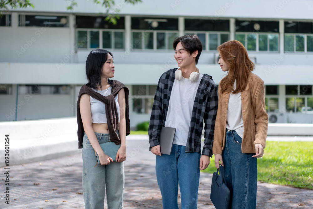 Three young people are walking together on a sidewalk, smiling and holding books