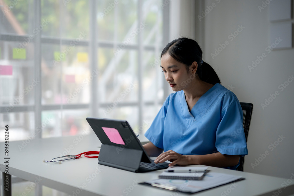 A woman in a blue scrubs is typing on a laptop A woman in a blue scrubs is typing on a laptop