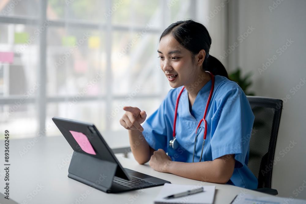 A woman in a blue scrubs is sitting at a desk with a tablet in front of her A woman in a blue scrubs is sitting at a desk with a tablet in front of her