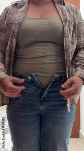 woman with their hands on belly, a girl tries to button her jeans, the girl's big belly prevents her from buttoning her jeans