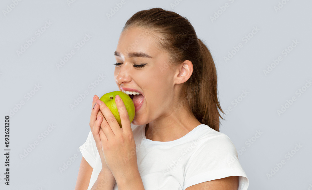 Young Lady Biting Green Apple Standing Over White Background. Healthy Snack Concept. Studio Shot, Isolated Young Lady Biting Green Apple Standing Over White Background. Healthy Snack Concept. Studio Shot, Isolated