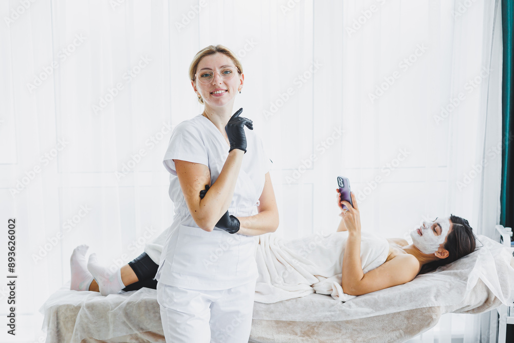 Obraz premium A cosmetologist wearing glasses and gloves performs a facial care procedure on a patient. A professional woman cosmetologist in a white coat with a well-lit office.