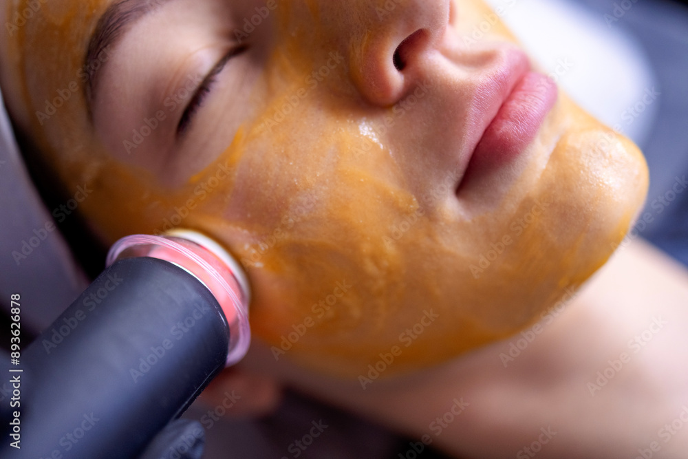 A young woman in a bathrobe lies and receives a facial cleansing procedure using a device A young woman in a bathrobe lies and receives a facial cleansing procedure using a device