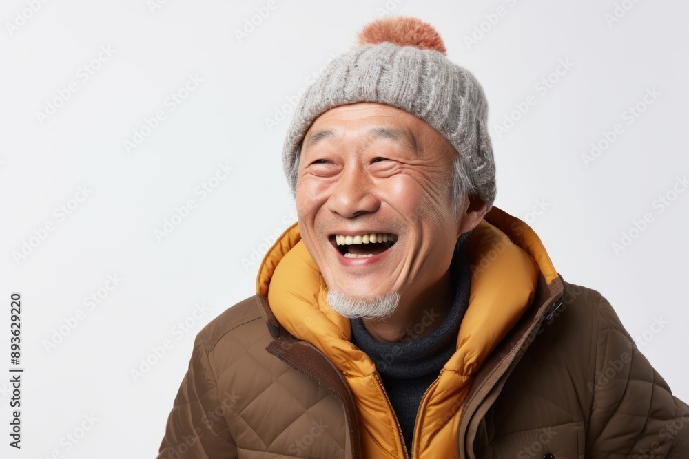 Portrait of a joyful asian man in his 60s dressed in a warm ski hat in front of white background Portrait of a joyful asian man in his 60s dressed in a warm ski hat in front of white background