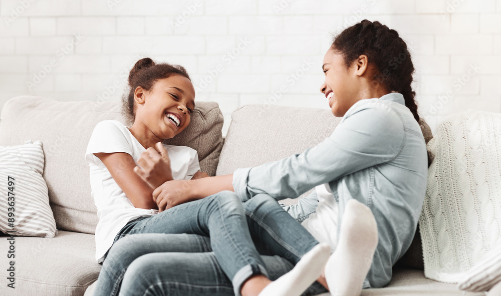 Lovely african sisters having fun together at home, sitting on sofa and laughing, copy space Lovely african sisters having fun together at home, sitting on sofa and laughing, copy space