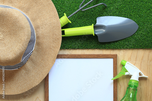 Gardening, composition of objects, flat lay. Gardening tool, frame for photo or text and summer hat on a background of grass and wood texture. World Environment Day. Top view. Spring gardening concept