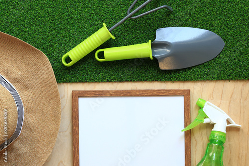 Gardening, composition of objects, flat lay. Gardening tool, frame for photo or text and summer hat on a background of grass and wood texture. World Environment Day. Top view. Spring gardening concept