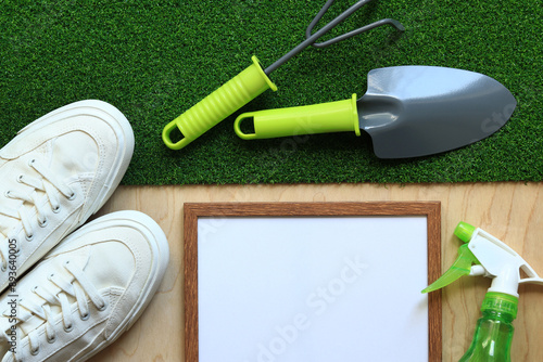 Gardening, composition of objects, flat lay. Gardening tool, frame for photo or text and white sneakers on a background of grass and wood texture. Spring gardening concept. Top view
