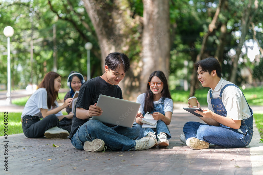 A group of five young adults is sitting together path in a park, engaged in a collaborative study session. A group of five young adults is sitting together path in a park, engaged in a collaborative study session.
