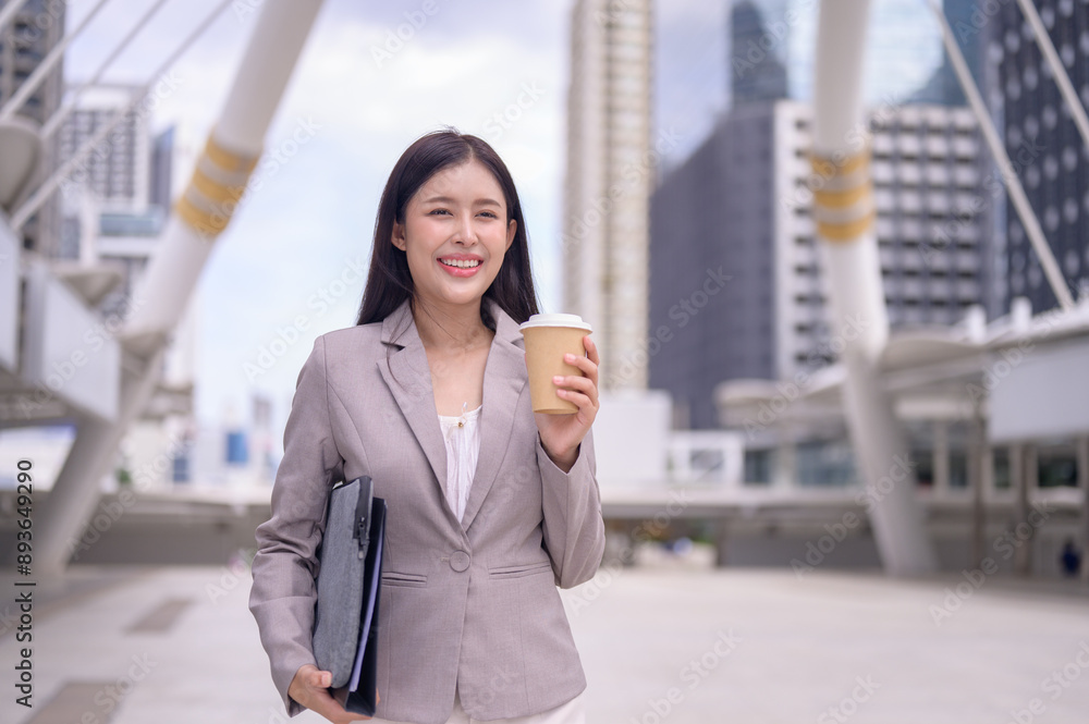 Confident young businesswoman holding a coffee cup standing among big city with modern skyscrapers. Confident young businesswoman holding a coffee cup standing among big city with modern skyscrapers.