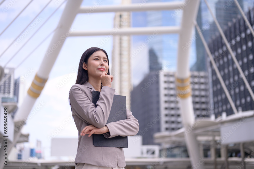 Professional businesswoman in formal suit standing outdoor against skyscrapers in the business district of the city and looking thoughtfully. Professional businesswoman in formal suit standing outdoor against skyscrapers in the business district of the city and looking thoughtfully.