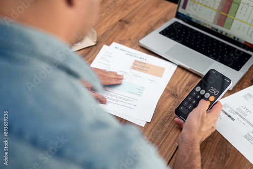 Fotografía Man using a smartphone calculator to review utility bills at a wooden table