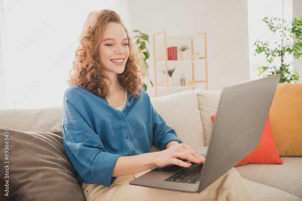 Photo of attractive trendy young woman sit sofa work netbook blue shirt move new apartment home interior indoors Photo of attractive trendy young woman sit sofa work netbook blue shirt move new apartment home interior indoors
