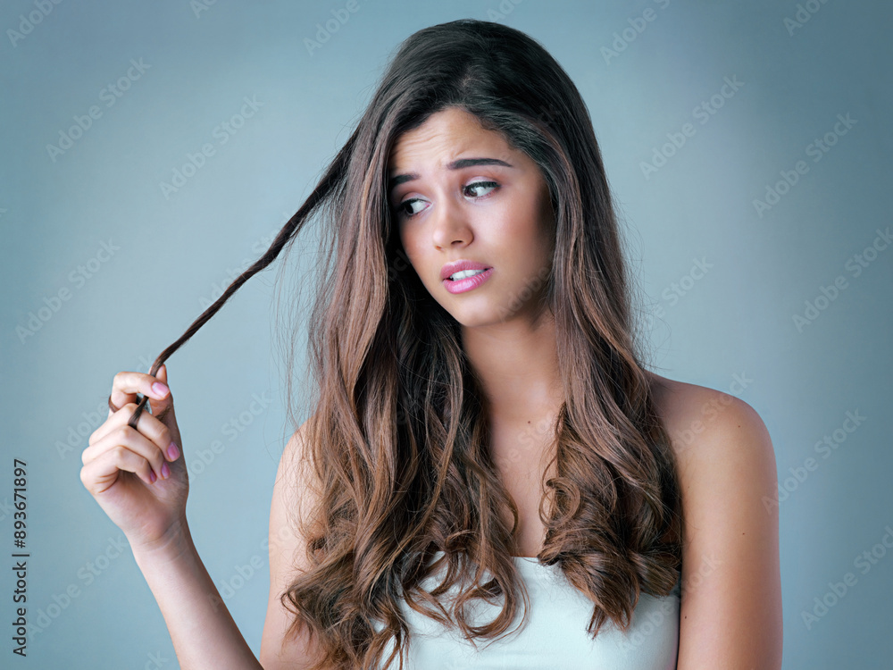 Fototapeta premium Treatment, damage and woman in studio with hair care, cosmetic results or checking split ends. Heat, texture and frustrated girl with hairstyle crisis, keratin therapy and thinking on blue background