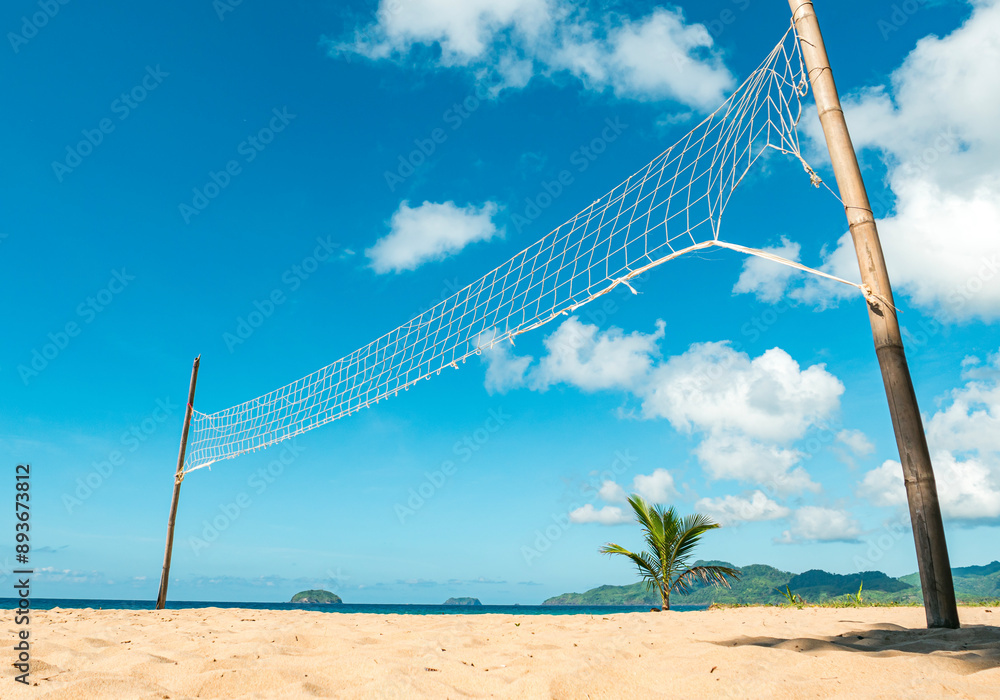 Beach volleyball net on sandy shore with palm tree and blue sky Beach volleyball net on sandy shore with palm tree and blue sky