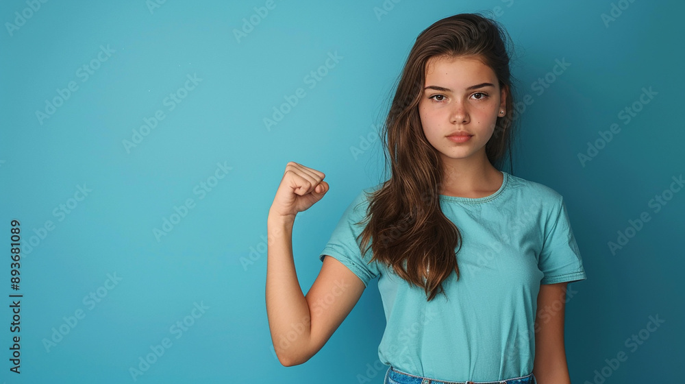 A teenage girl in a blue shirt, standing against a matching blue background, making a fist with a determined expression, symbolizing strength and determination. A teenage girl in a blue shirt, standing against a matching blue background, making a fist with a determined expression, symbolizing strength and determination.