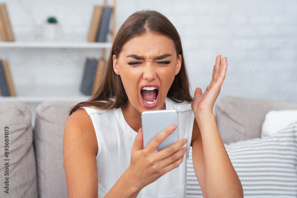 Phone Quarrel. Furious Lady Shouting On Smartphone Talking With Boyfriend Sitting On Couch At Home. Selective Focus Phone Quarrel. Furious Lady Shouting On Smartphone Talking With Boyfriend Sitting On Couch At Home. Selective Focus