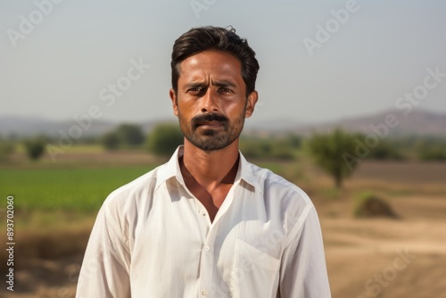 Portrait of a tender indian man in his 40s wearing a simple cotton shirt isolated in quiet countryside landscape