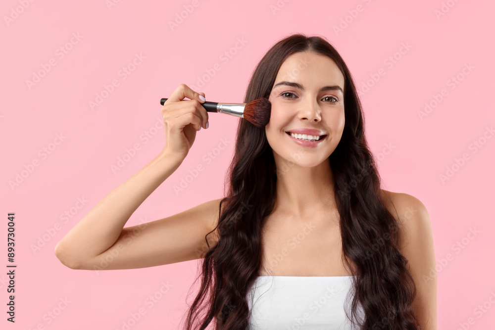 Smiling woman applying makeup with brush on pink background Smiling woman applying makeup with brush on pink background