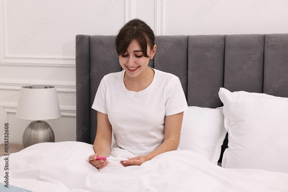 Happy young woman with pregnancy test on bed at home Happy young woman with pregnancy test on bed at home