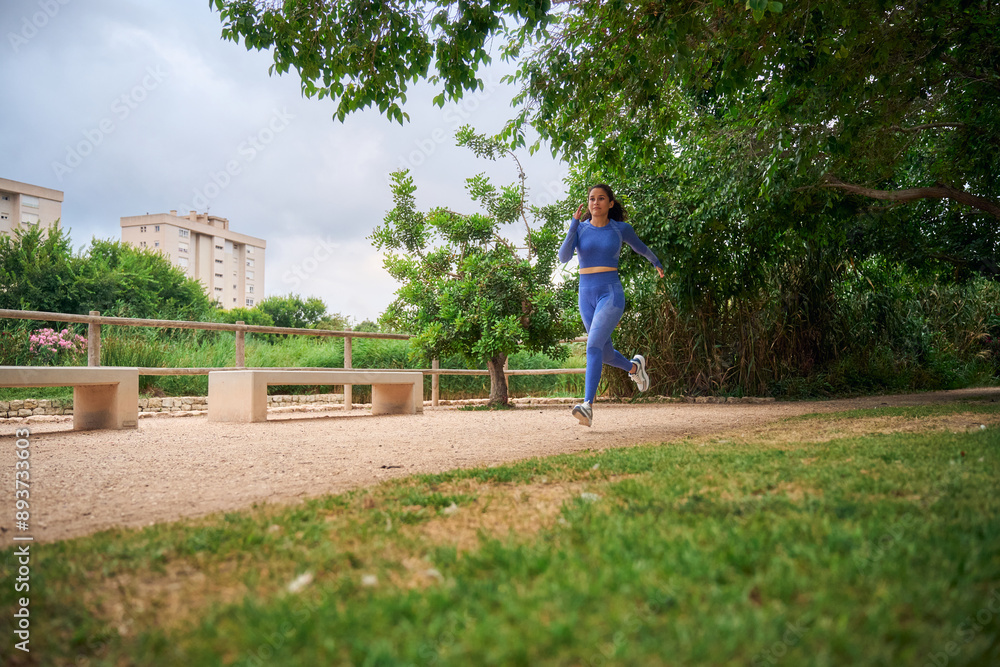 Woman running in blue activewear through a park on a cloudy day Woman running in blue activewear through a park on a cloudy day