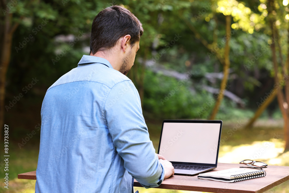 Freelancer working with laptop at table in forest, back view. Remote job Freelancer working with laptop at table in forest, back view. Remote job