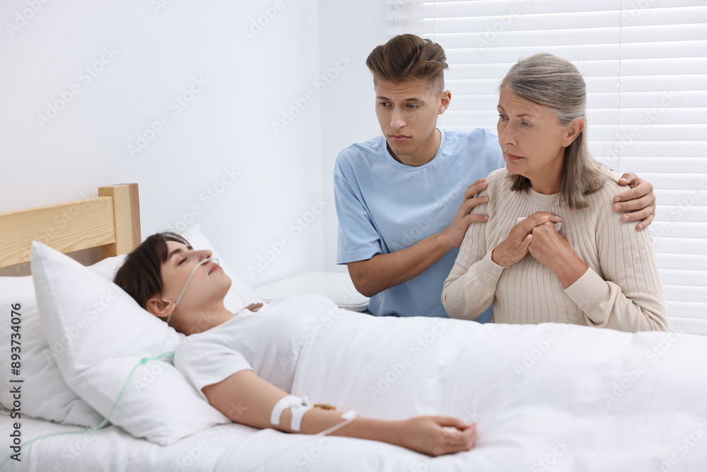 Coma patient. Sad relatives near sleeping young woman in hospital Coma patient. Sad relatives near sleeping young woman in hospital